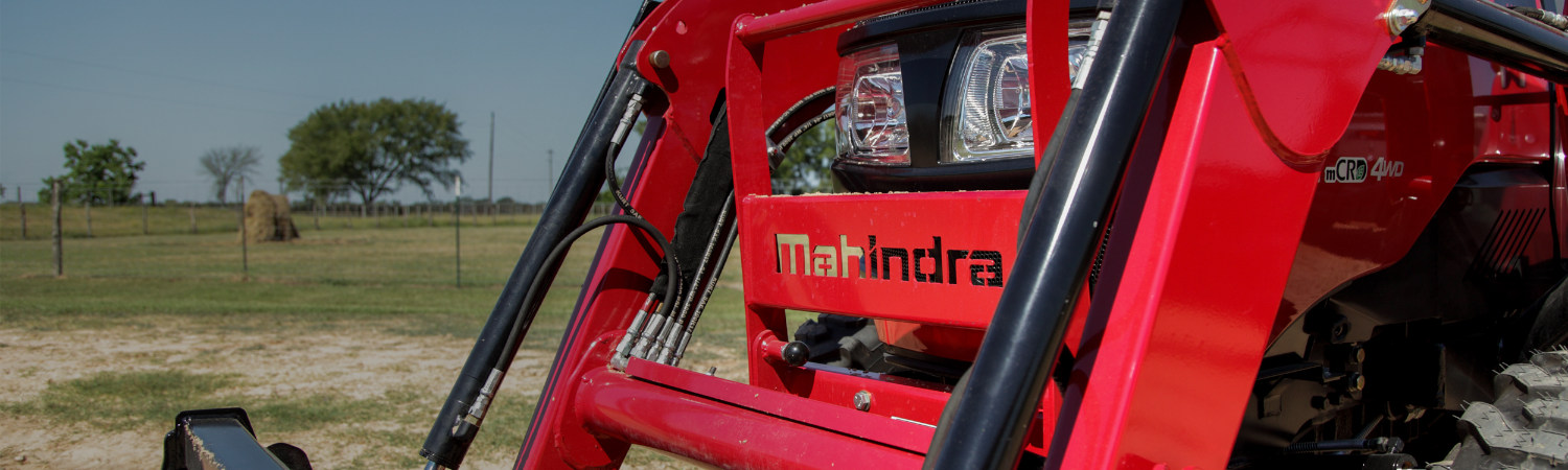 A Mahindra® tractor sitting on a farm underneath a blue sky.